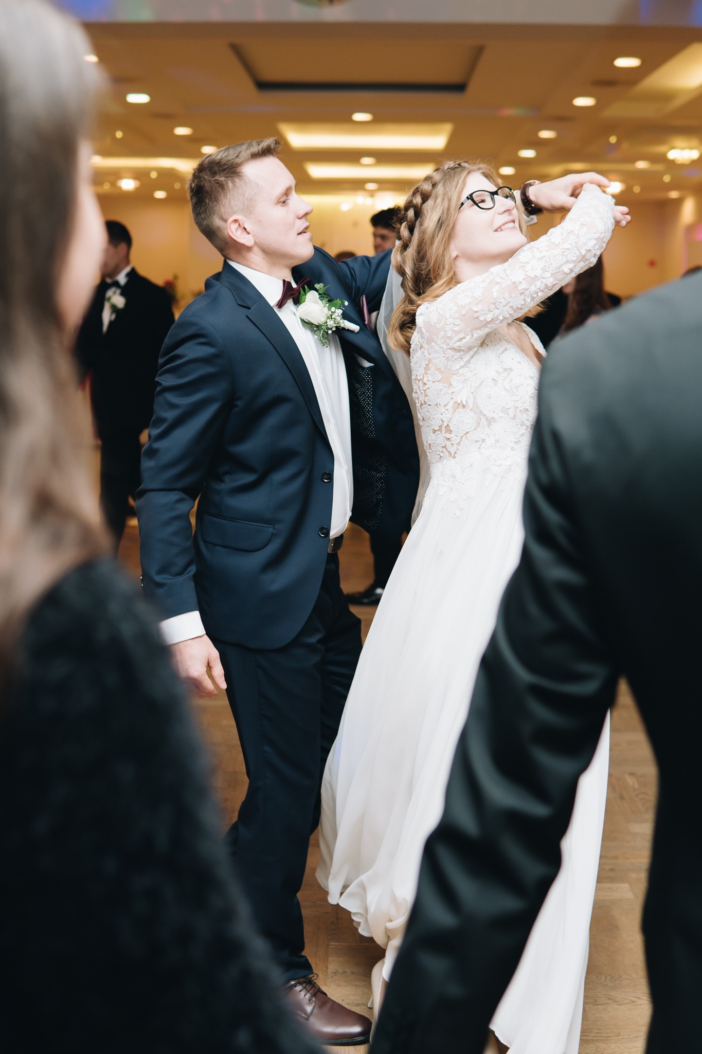 Para młoda w trakcie tańca podczas wesela w Warszawie, panna młoda w okularach i koronkowej sukni, pan młody w granatowym garniturze z bordową muchą.