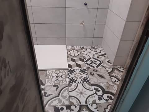 Fragment łazienki w trakcie remontu, widoczne ułożone płytki podłogowe we wzory retro, białe płytki ścienne i biała płytka podłogowa przygotowana do ułożenia.