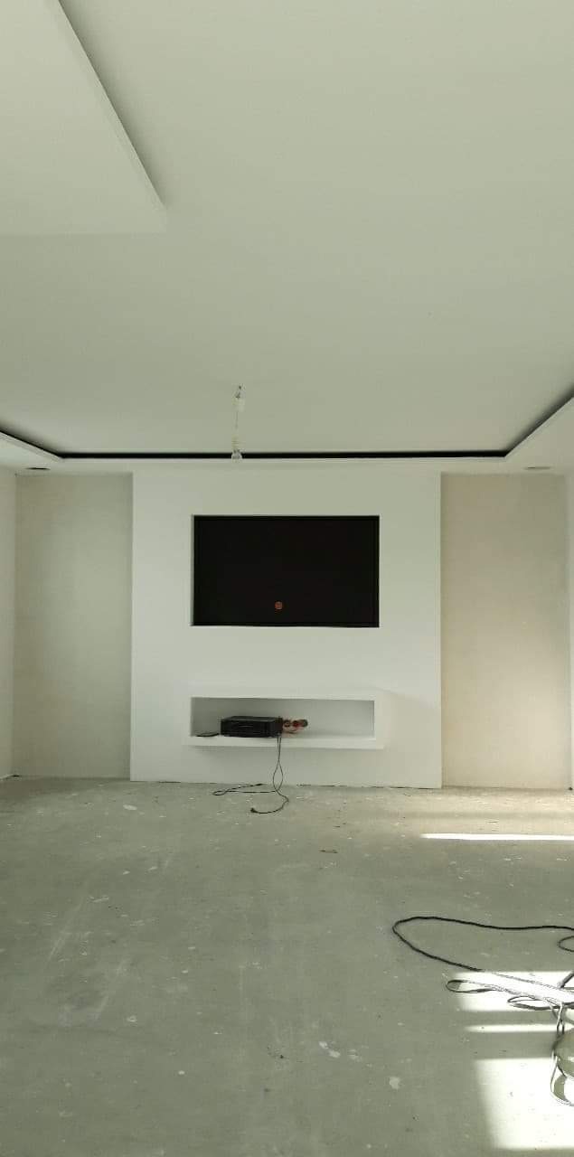 Świeżo wykończone wnętrze z wnęką na telewizor i półką pod spodem, surowy beton na podłodze, widoczne kable, minimalistyczny design.