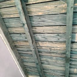 T.P Usługi Tomasz Piszczek - Drewniana konstrukcja poddasza z naciągniętym sznurkiem, przygotowana do ocieplenia. Widoczne deski w odcieniach zieleni i beżu oraz biały sznurek tworzący siatkę.