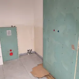 Montaż płyty gipsowej w łazience w Orońsku. Widoczne przygotowane ściany pod płytki, zabudowa stelaża WC. Podłoga wyłożona płytkami w odcieniach szarości.