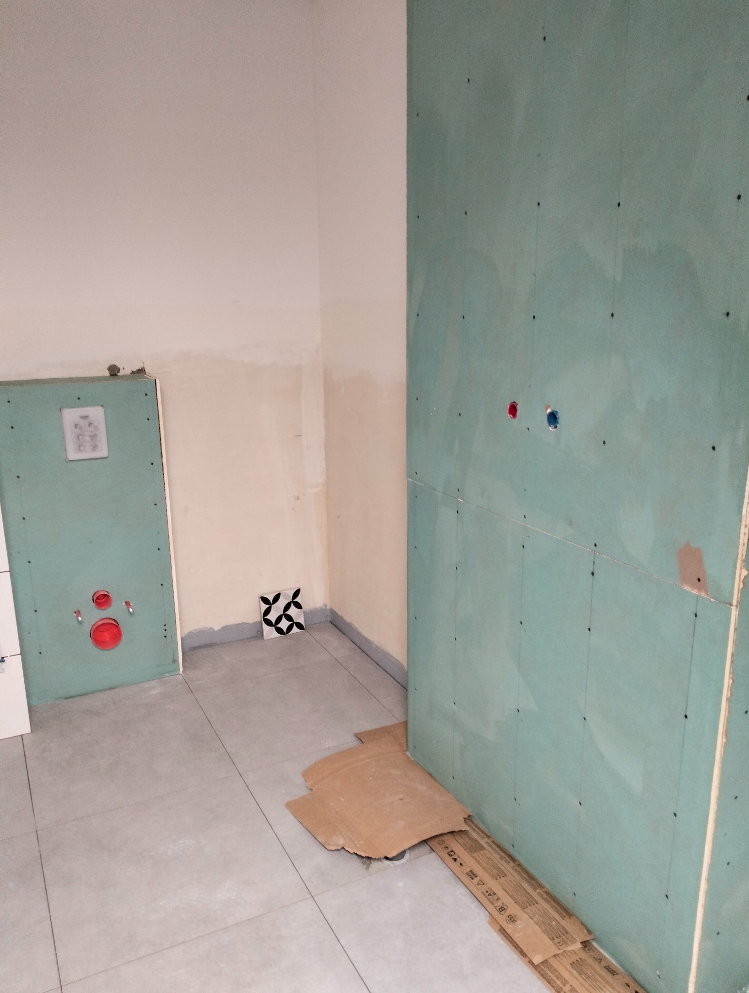 Montaż płyty gipsowej w łazience w Orońsku. Widoczne przygotowane ściany pod płytki, zabudowa stelaża WC. Podłoga wyłożona płytkami w odcieniach szarości.