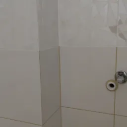 Fragment ściany w łazience z białymi płytkami, dolna część gładka, górna z geometrycznym wzorem, widoczne przyłącze wodne.