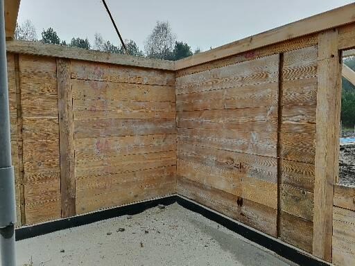 Surowe drewniane ściany szkieletowe budynku w trakcie budowy, widoczne ślady po wstępnej obróbce drewna, zarys czarnej izolacji poziomej