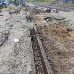 AAP Budownictwo Volodymyr Keryk - Przygotowanie szalunku i zbrojenia pod wylewkę fundamentu, widoczny laserowy niwelator wyznaczający poziom, narzędzia budowlane w tle, teren budowy.