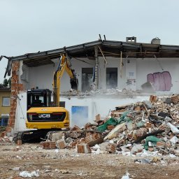 AAP Budownictwo Volodymyr Keryk - Żółta koparka JCB podczas rozbiórki budynku z białymi ścianami, widoczne gruzy i elementy konstrukcyjne, graffiti na ścianie.