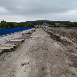 AAP Budownictwo Volodymyr Keryk - Rozbiórka mostu w toku: zerwana nawierzchnia, gruz, fragmenty betonowe, w tle koparka i zieleń. Widok z perspektywy jezdni.