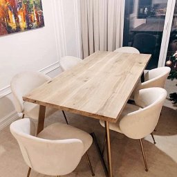 Hardwood Classic - Stół z blatem z jasnego drewna o wyraźnym usłojeniu, wsparty na złotych, skośnych nogach, otoczony przez sześć kremowych krzeseł z welurową tapicerką i złotymi nogami, w tle obraz i zasłony.