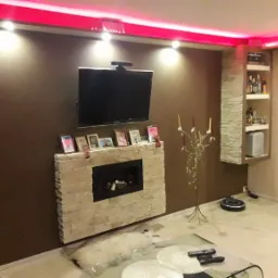 Salon z kominkiem obłożonym kamieniem, telewizorem na ścianie, podświetleniem LED na suficie i wbudowaną półką na alkohol z dekoracyjną okładziną z kamienia.