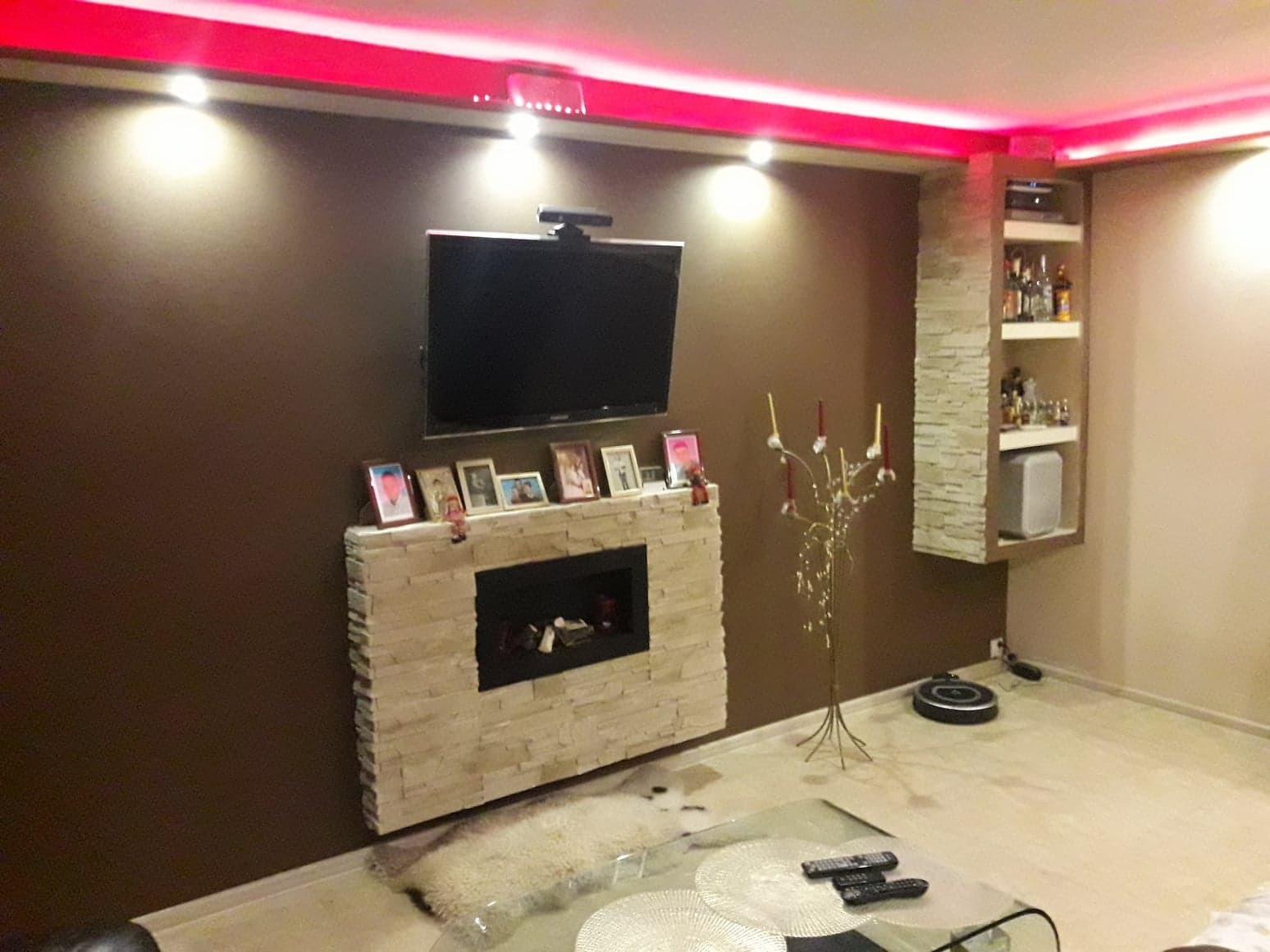 Salon z kominkiem obłożonym kamieniem, telewizorem na ścianie, podświetleniem LED na suficie i wbudowaną półką na alkohol z dekoracyjną okładziną z kamienia.