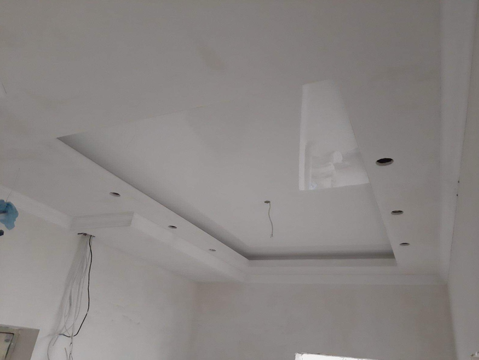 Biały sufit podwieszany z wnęką i otworami na oświetlenie punktowe, widoczne kable i przewody elektryczne.