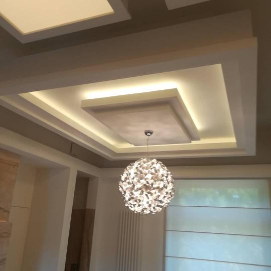 Wykończony sufit podwieszany z oświetleniem LED i dekoracyjnym żyrandolem w nowoczesnym wnętrzu.