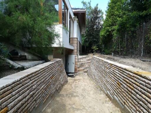 Kamienna ścieżka prowadząca do wejścia domu z białymi ścianami i dużymi oknami, otoczona zielenią.