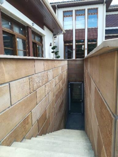 Zewnętrzne schody prowadzące do piwnicy budynku z elewacją z piaskowca, widoczne okna z brązowymi ramami i fragment dachu.