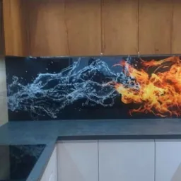 Białe szafki kuchenne z ciemnoszarym blatem i panelem szklanym nad blatem, przedstawiającym motyw wody i ognia.