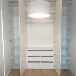 Wnętrze białej szafy wnękowej z otwartymi drzwiami, widoczne półki i sześć szuflad, oświetlenie sufitowe.