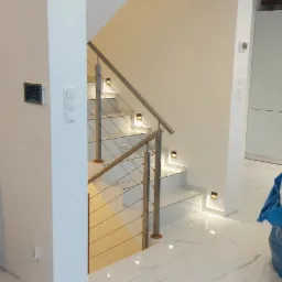 Nowoczesne, oświetlone schody z metalową balustradą i białymi stopniami w jasnym wnętrzu z marmurową podłogą.