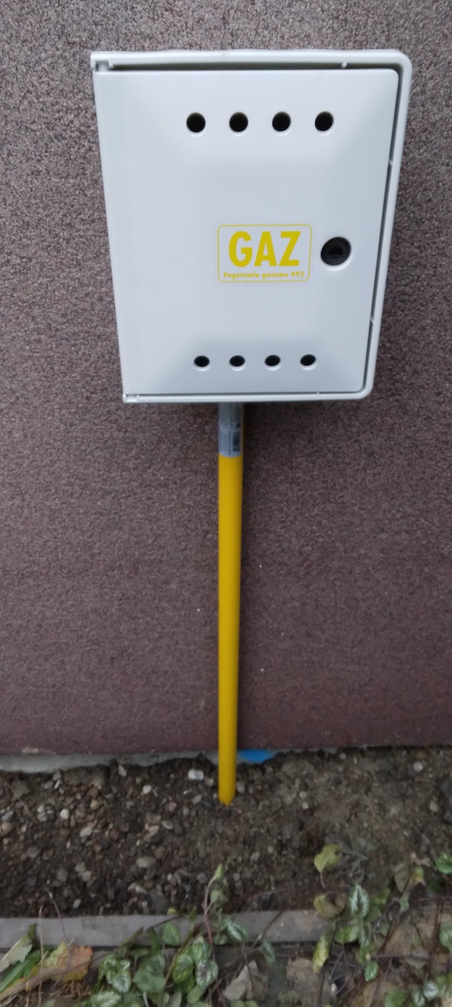 Żółta rura gazowa w Opocznie, prowadząca do białej skrzynki gazowej na ścianie budynku.