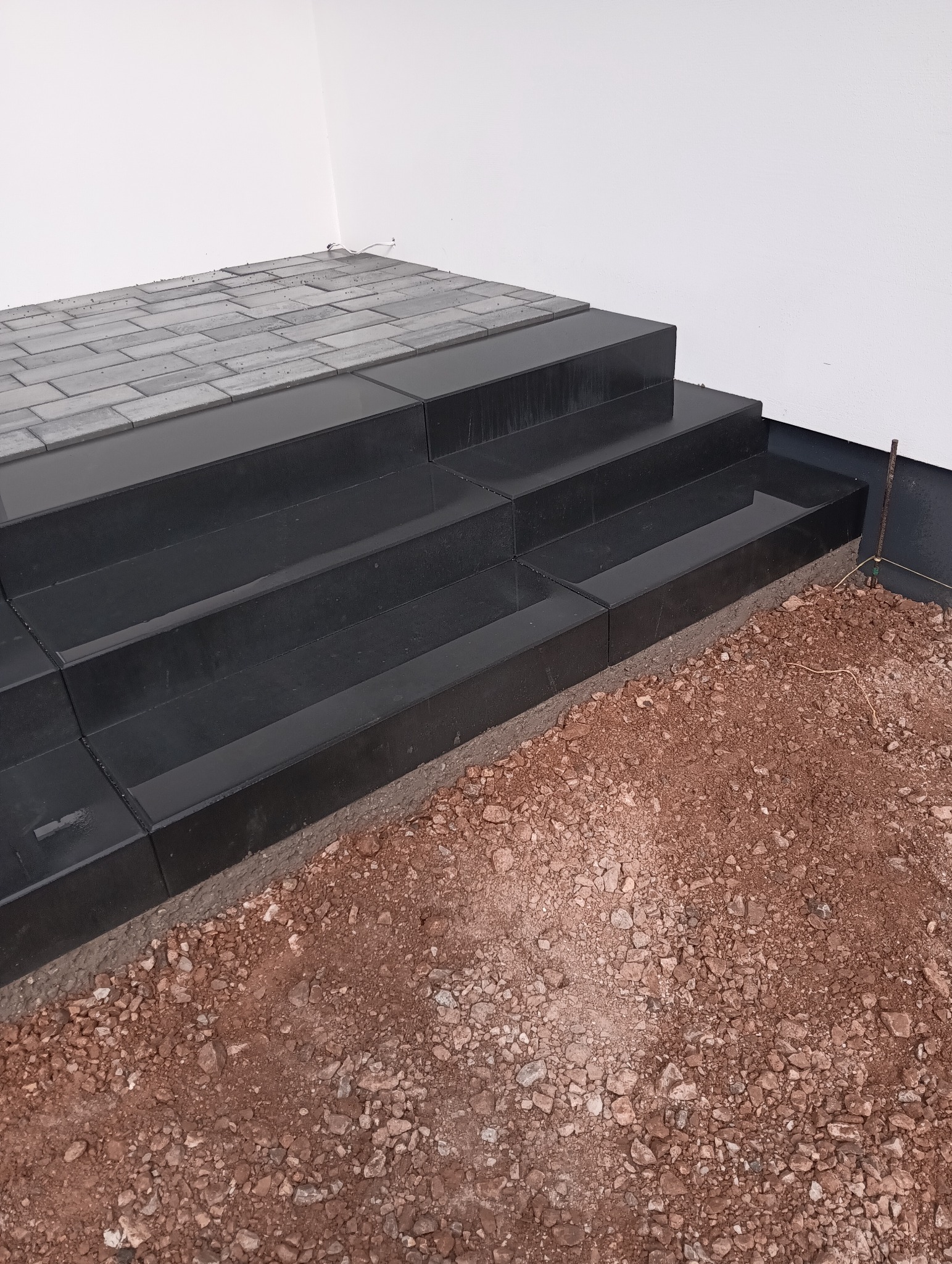 Ciemne, eleganckie schody z kostki brukowej prowadzące do budynku, otoczone ziemią. Widoczne detale łączeń i faktura materiału.