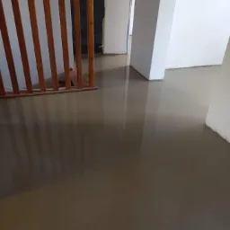 Wylany samopoziomujący podkład podłogowy w jasnym pomieszczeniu, widoczny drewniany ażurowy przepierzenie i białe ściany w tle.