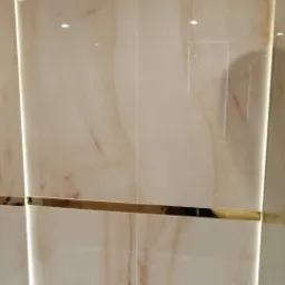 Beżowe płytki imitujące marmur z dekoracyjnym złotym paskiem i deszczownicą w wykończonej łazience we Wrocławiu.