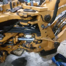 Żółta, hydrauliczna część koparko-ładowarki Case 590sr w trakcie naprawy, widoczne przewody hydrauliczne, siłownik i narzędzia.