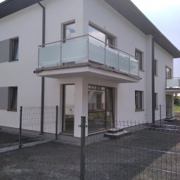 Kristal - Nowoczesny budynek z balkonami zabezpieczonymi szklanymi balustradami ze stalowymi poręczami, widok z zewnątrz przez metalowe ogrodzenie.