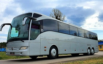 Srebrny autokar turystyczny z numerem bocznym 35 na tle zieleni i błękitnego nieba z chmurami.