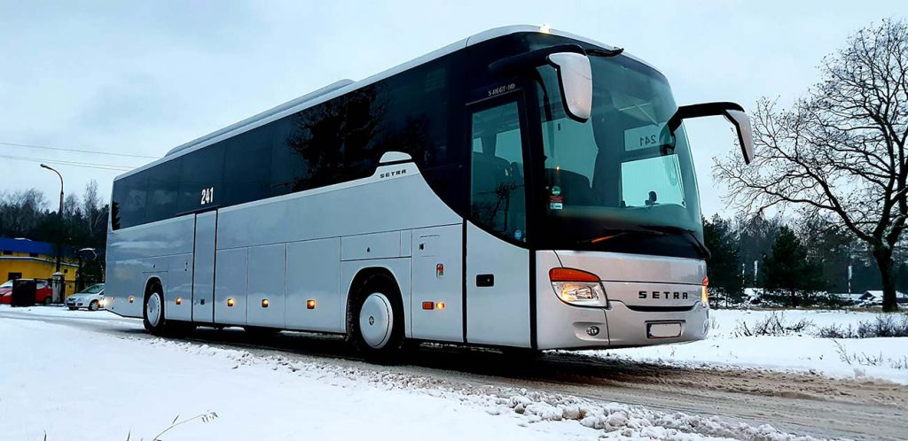 Nowoczesny, srebrny autokar marki Setra, numer boczny 241, zaparkowany na ośnieżonej drodze, widok z boku na tle zimowego krajobrazu.