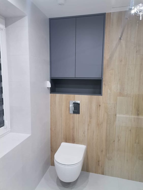 Nowoczesna łazienka z podwieszaną toaletą, drewnopodobną okładziną ściany, szarą szafką wiszącą i chromowanym przyciskiem spłuczki.