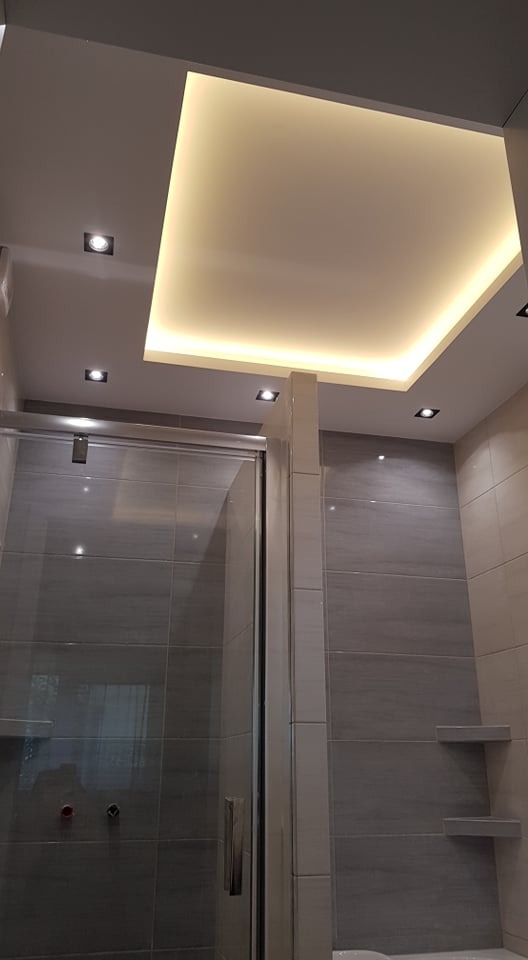 Nowoczesna łazienka z szarą glazurą, kabiną prysznicową i podwieszanym sufitem z oświetleniem LED oraz punktowymi lampami.