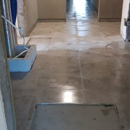 Stanisław Piersa - Korytarz w trakcie prac wykończeniowych, świeżo położona szara terakota na podłodze, widoczne niedokończone ściany i instalacje.