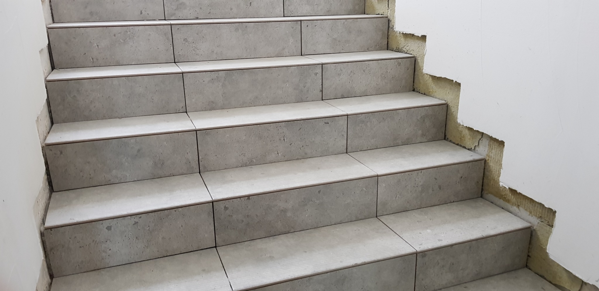 Układanie płytek na schodach w Olsztynie, widoczne niedokończone wykończenie ściany obok.