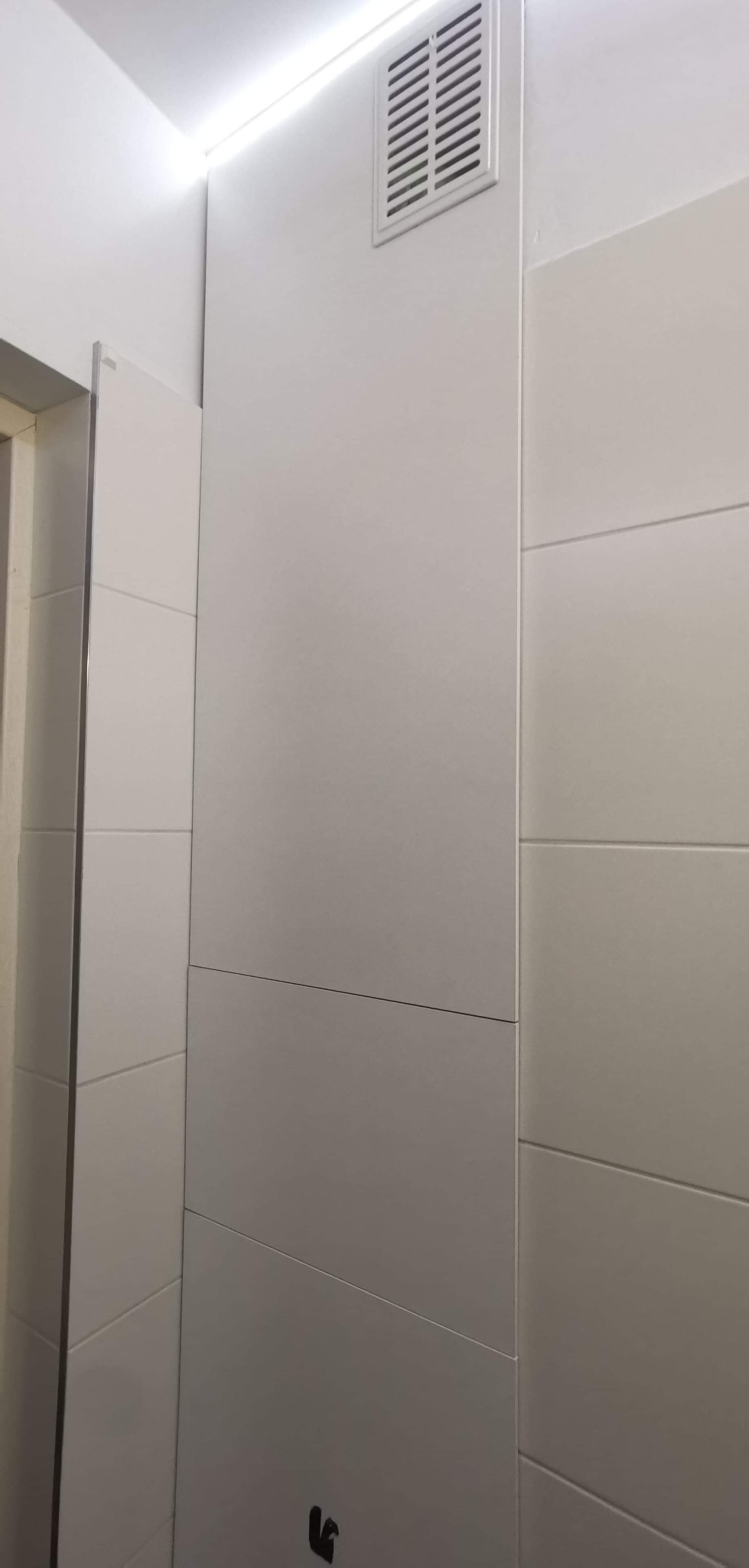 Biała szafa wnękowa z matowymi frontami, minimalistycznym designem i kratką wentylacyjną w górnej części.