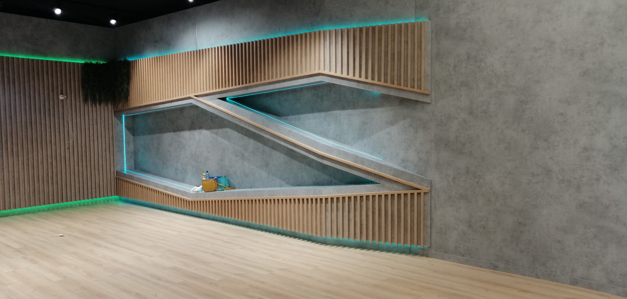 Nowoczesne wnętrze z drewnianymi lamelami i podświetlanymi półkami o nietypowym kształcie, na podłodze panele, widoczne akcesoria malarskie.