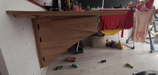 Zamontowany blat drewniany w Poznaniu, przymocowany do ściany za pomocą drewnianej konstrukcji wsporczej o trójkątnym kształcie, widoczne zabawki dziecięce na podłodze i suszarka z praniem w tle.