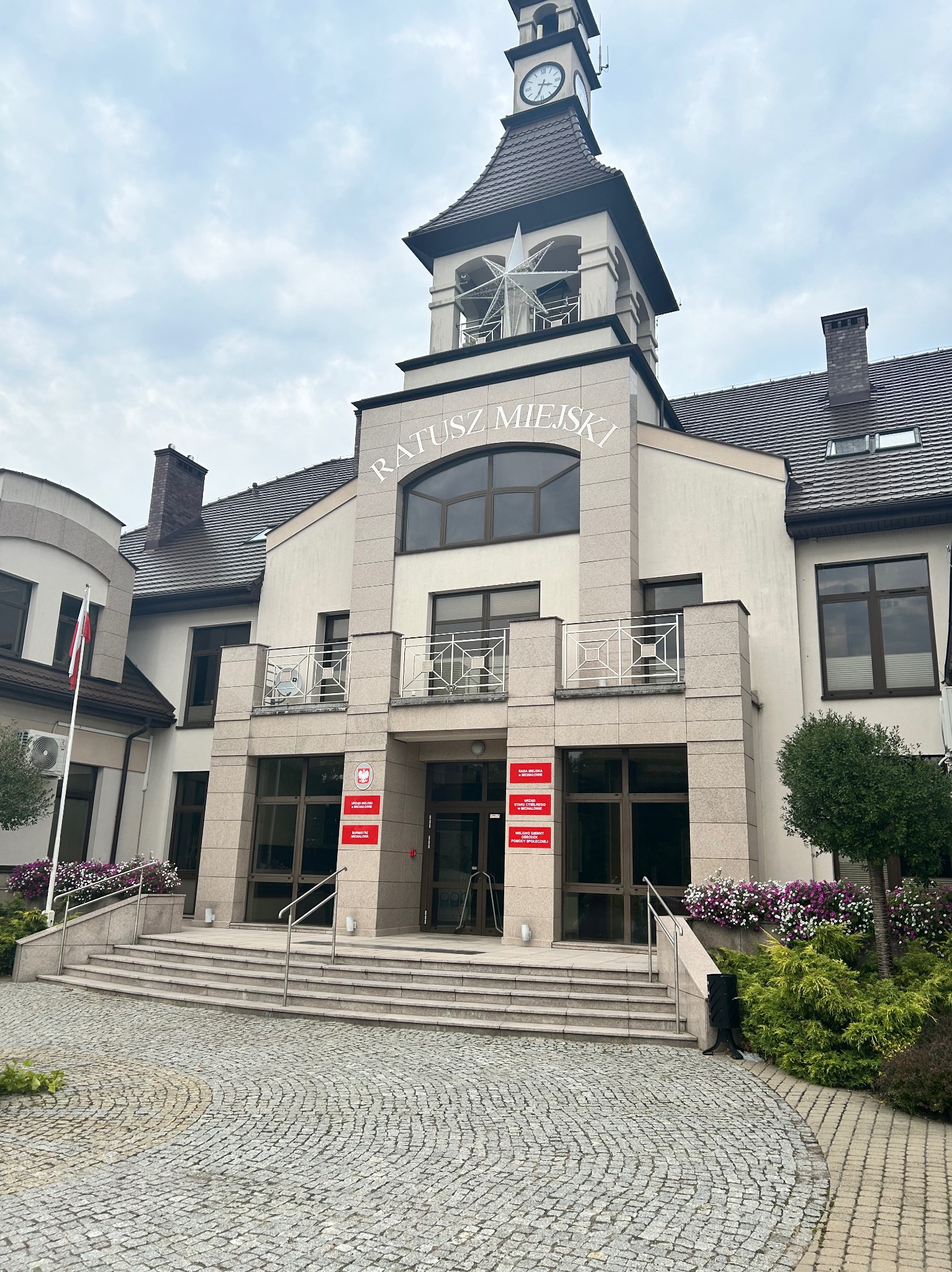 Fasada Ratusza Miejskiego z wieżą zegarową, widoczne okna, schody wejściowe i bruk.