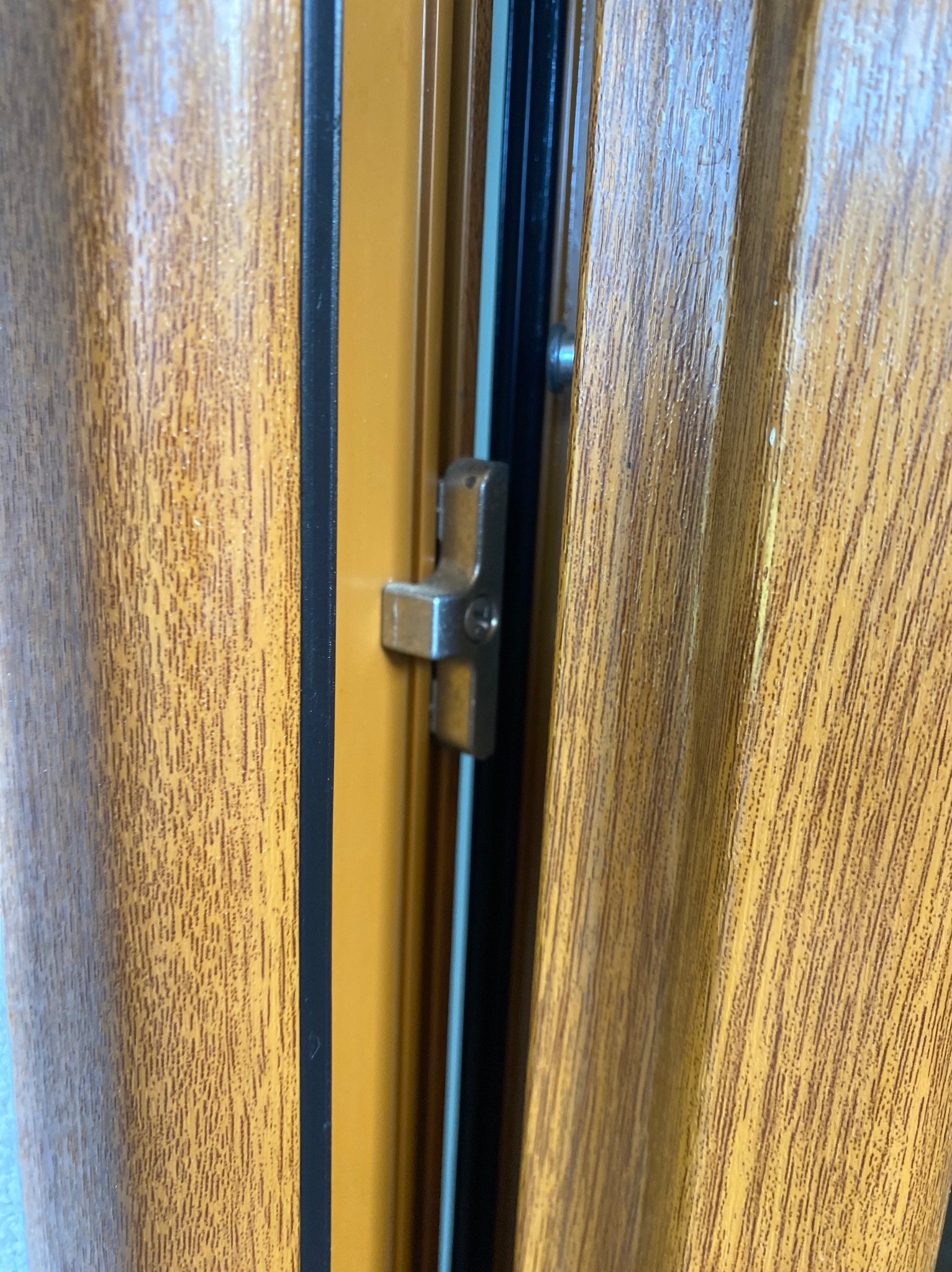 Zamknięcie okienne w oknie z okleiną drewnopodobną w odcieniach brązu i beżu, widoczne detale uszczelki i ramy.