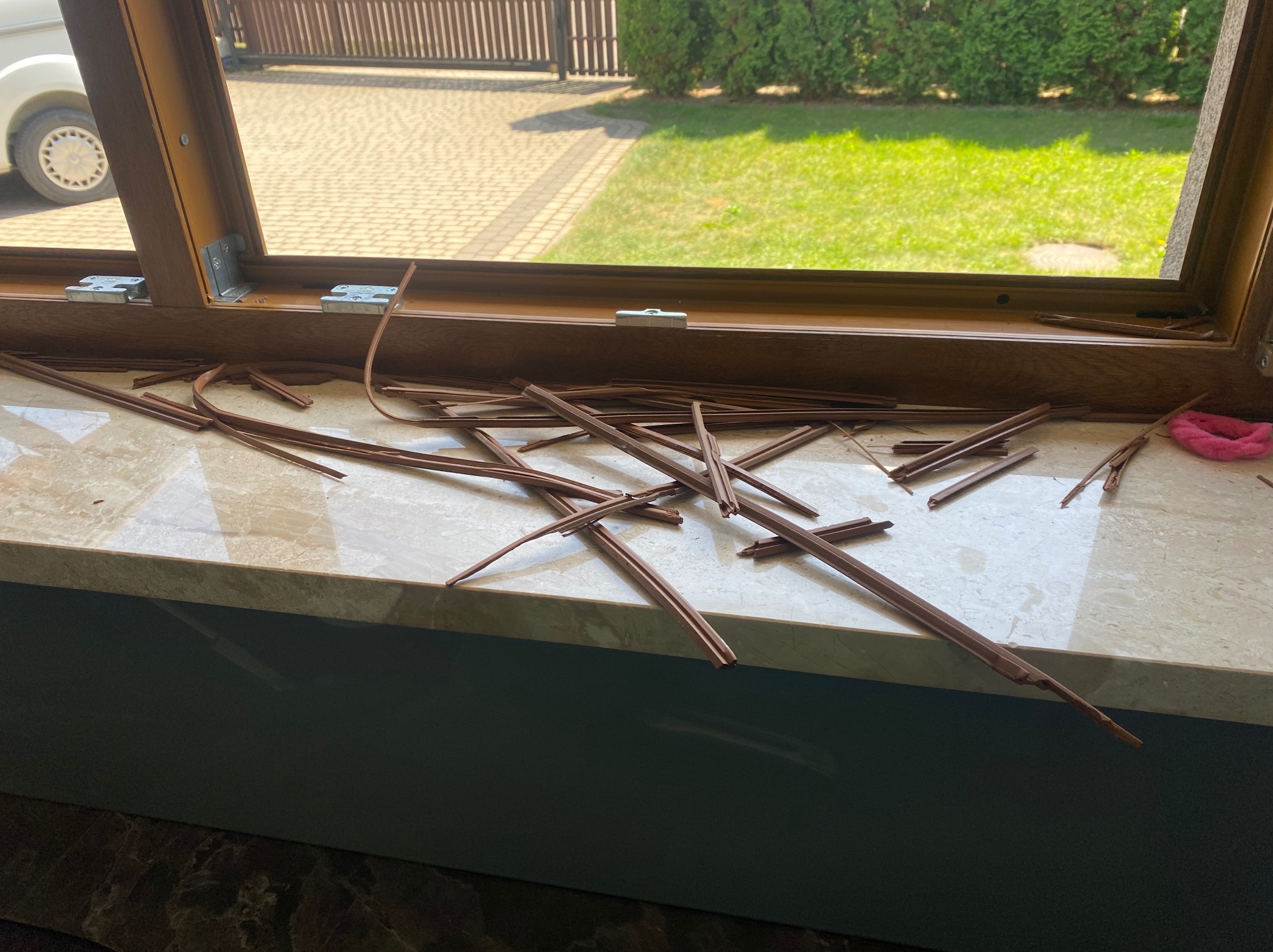 Demontaż listew przyszybowych okna PCV podczas naprawy, widoczne elementy okna, usunięte listwy i fragment widoku na zewnątrz.