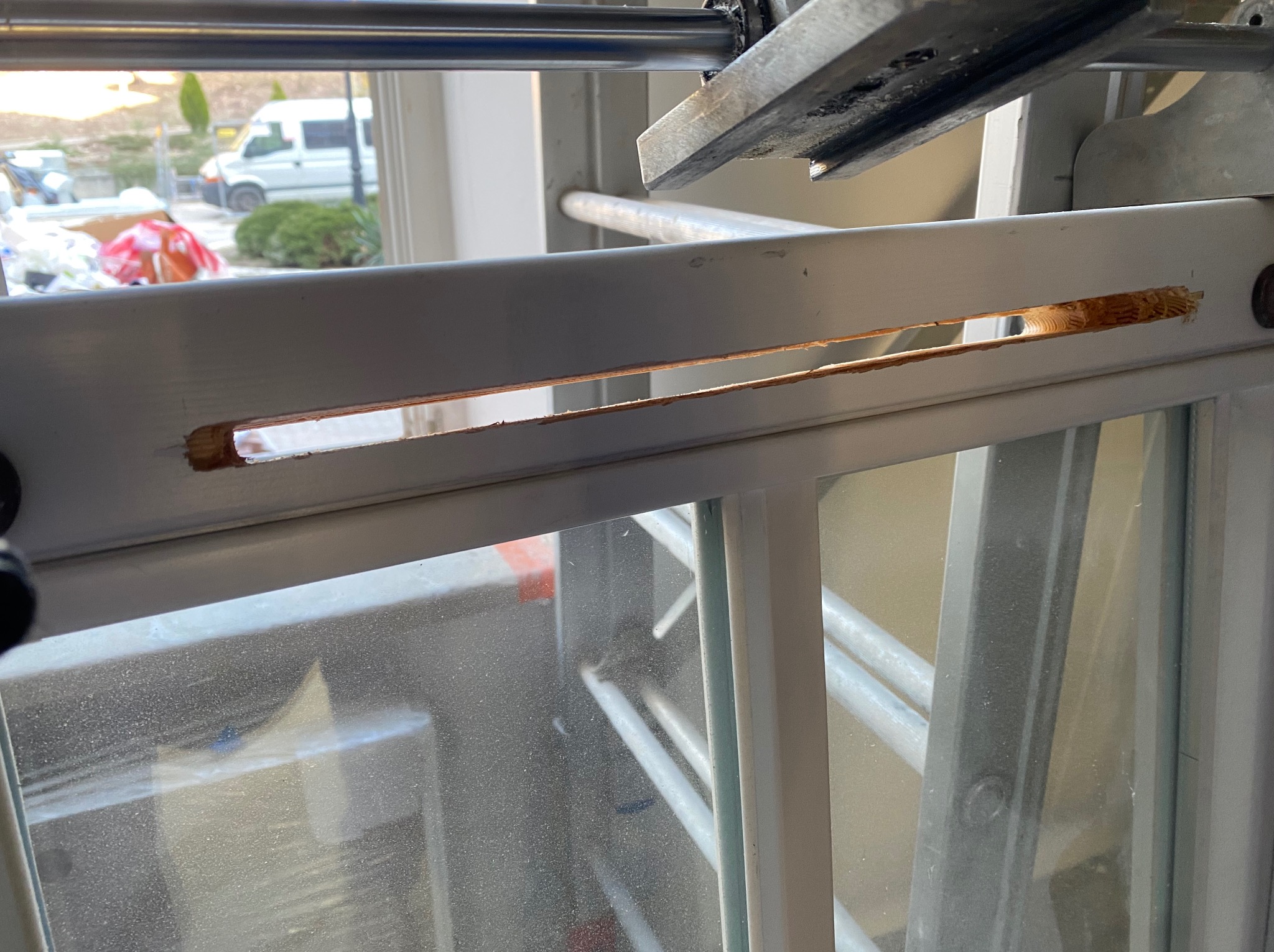 Uszkodzona rama okienna z widocznym ubytkiem drewna, prawdopodobnie po próbie włamania, z zewnątrz widoczny fragment drabiny i samochód dostawczy