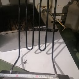 Id-Serwice Sp. z o.o. - Wyjęta grzałka z piekarnika, widoczne ślady przypaleń i zabrudzeń, obok leży miarka, tło stanowi biały blat i wnętrze piekarnika.