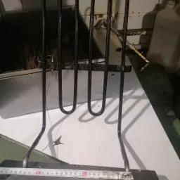 Wyjęta grzałka z piekarnika, widoczne ślady przypaleń i zabrudzeń, obok leży miarka, tło stanowi biały blat i wnętrze piekarnika.