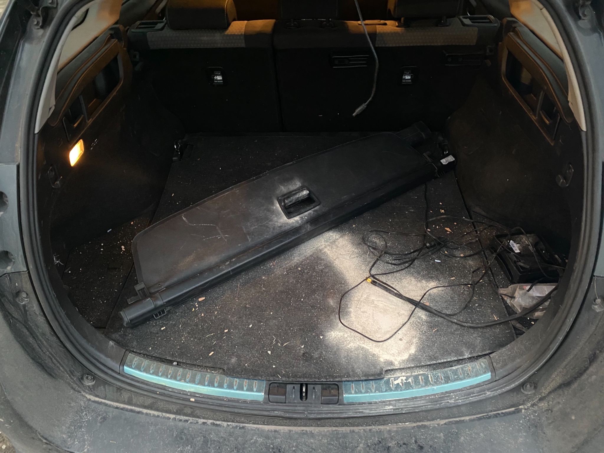 Brudny bagażnik samochodu z roletą, kablami i drobnymi zanieczyszczeniami na dywaniku.