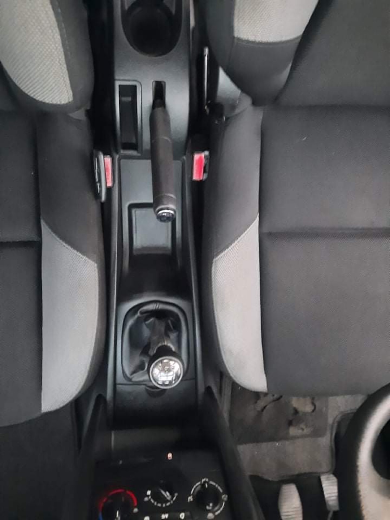 Wnętrze samochodu z widocznymi szarymi fotelami z ciemnymi bokami, dźwignią zmiany biegów i hamulcem ręcznym, uchwycone z góry.