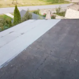 Widok z góry na fragment dachu po hydroizolacji w Gidlach, z widocznym połączeniem starej i nowej powłoki, w tle zabudowania mieszkalne i zieleń.