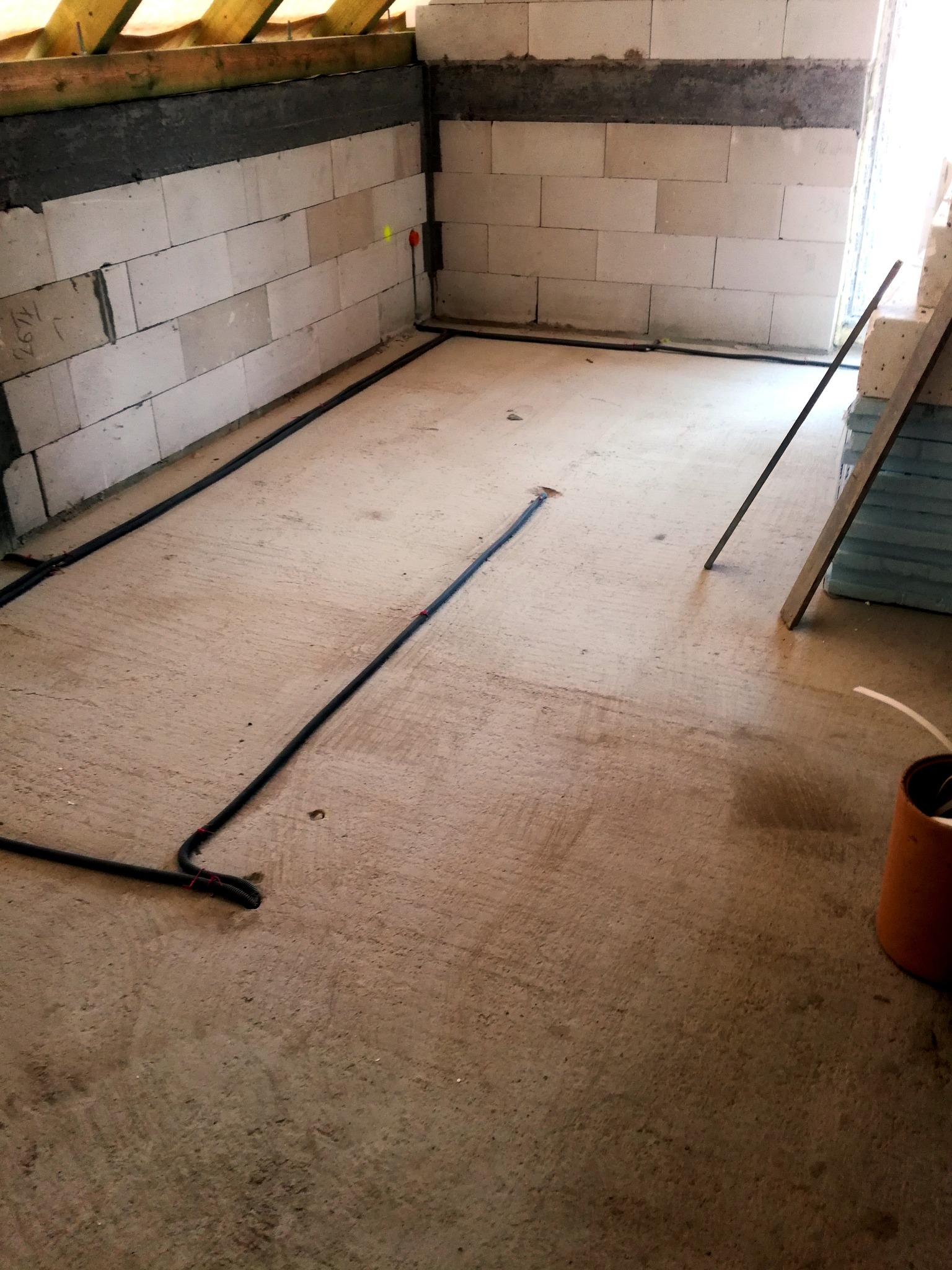 Surowy stan podłogi w trakcie prac instalacyjnych: widoczne przewody elektryczne prowadzone po betonowej posadzce, ściany z betonu komórkowego, drewniana konstrukcja stropu, składowane płyty...