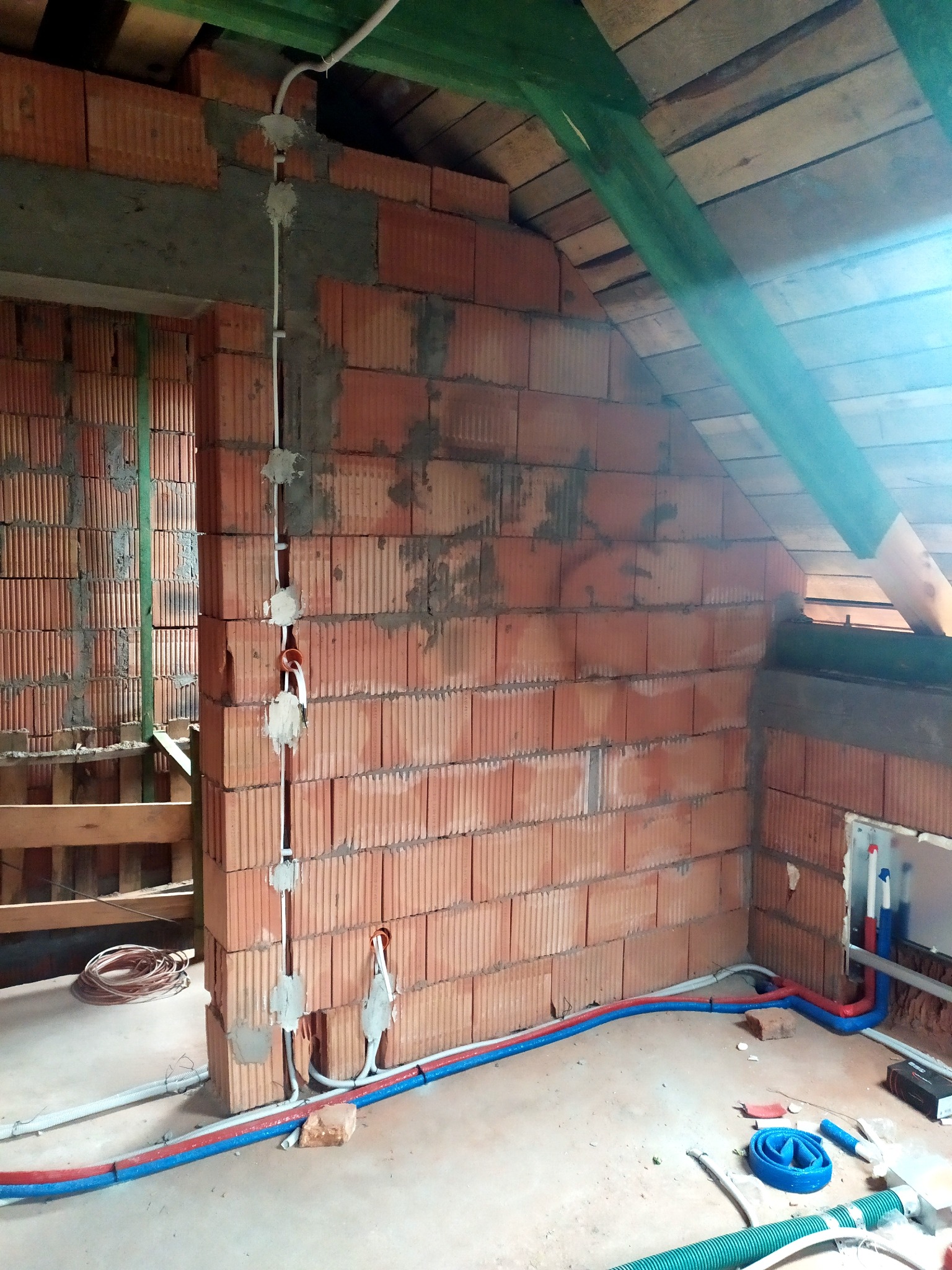 Instalacja elektryczna w trakcie montażu w surowym wnętrzu poddasza, widoczne kable prowadzone po ceglanej ścianie i pod sufitem, z puszkami instalacyjnymi częściowo zamaskowanymi gipsem, oraz rury...