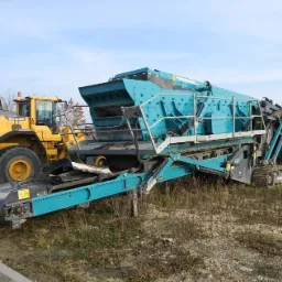 Żółta ładowarka Volvo obok niebiesko-czarnego przesiewacza mobilnego Powerscreen na nierównym terenie.