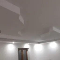 Nowoczesny sufit z nieregularnymi elementami dekoracyjnymi i oświetleniem punktowym w białym wnętrzu.