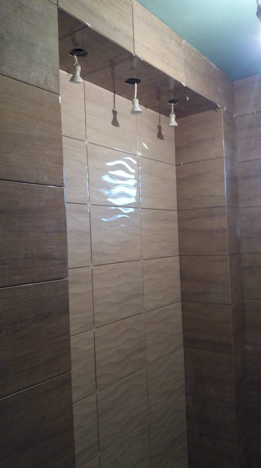 Wykończona wnęka prysznicowa z beżowymi i brązowymi płytkami ceramicznymi z delikatnym wzorem fal, przygotowana do montażu oświetlenia punktowego.